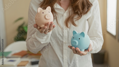 Fotografie Woman in white shirt holds pink and blue piggy banks in open hands inside building, comparing savings options; savings choice hopeful