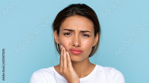 Upset young woman holding her cheek with tooth pain expression isolated on blue background, representing dental problems, oral healthcare, and sensitivity.
