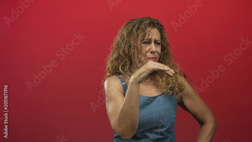 Foto Woman pinches nose with hand in studio red backdrop wearing a denim sleeveless top and grimacing; disgust aversion smell