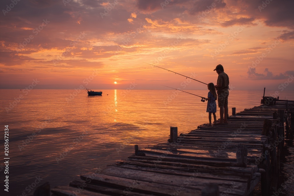 Fototapeta premium Father teaches his daughter to fish from a weathered wooden pier at sunset