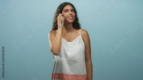 Schilderij op canvas Hispanic woman holding smartphone to ear with eyes closed wearing white sundress with embroidered hem in studio; calm reflection