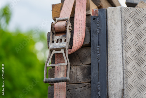 Картината върху платно Industrial ratchet tie down strap securing stacked wooden beams on a constructio