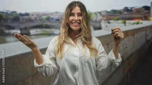 Foto Woman holds creditcard in hand and pumps fist while smiling on bridge street by the river; triumph confidence