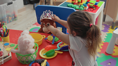Photography Hispanic girl placing tiara on stuffed monkey with outstretched arm at play table in building; imaginative play joy