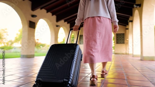 Asian woman walking through a train station with her suitcase.
