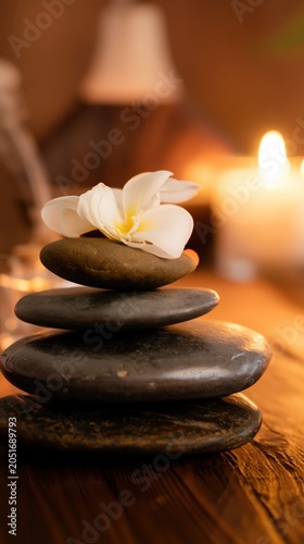 A serene spa still life with stacked stones and a plumeria flower on warm wood. Candlelight and diffused glow evoke relaxation, balance, and quiet luxury.