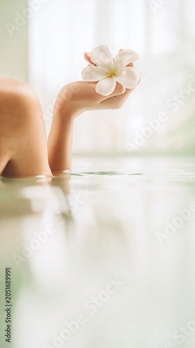 A minimalist spa scene highlights a relaxed hand with a white flower above tranquil water. Soft natural light enhances the serene and pure wellness ambiance.