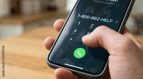 Close up of hand dialing addiction helpline on smartphone. Person seeking help and support for gambling problem. Pressing green call button on mobile phone screen