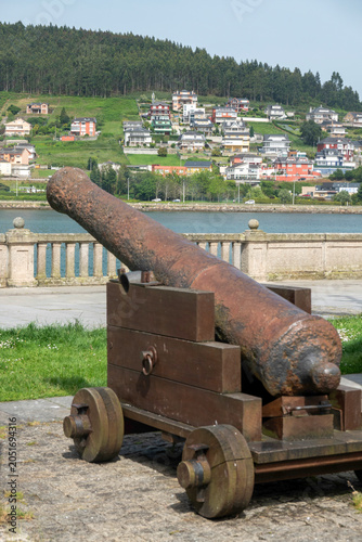 Ancient rusty cannon on a wooden carriage overlooking the estuary and hills in Viveiro, Lugo, Galicia, Spain.