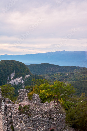 Fragment of a ruined castle silhouetted against sunset over mountain range. Dramatic historical landscape, golden hour atmosphere.