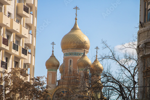 Golden domes of a Russian Orthodox church rising between residential buildings in Bucharest, Romania. Religious architecture featuring traditional Eastern Orthodox design
