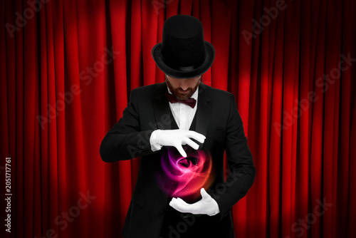 Fotografie Magician performing trick on stage with red curtains