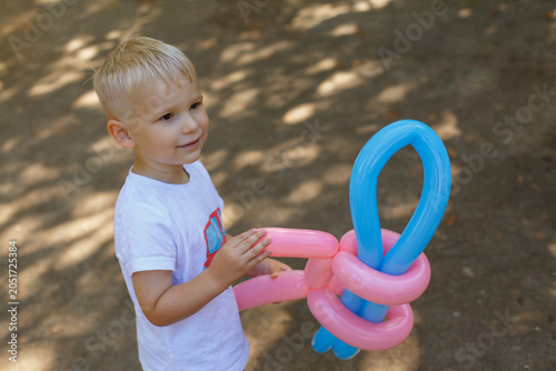 Toddler boy holding colorful balloon sculpture outdoors in summer park