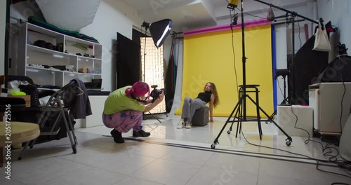 Female Photographer with Pink Hair Directs and Photographs a Female Model in a Modern Photo Studio with Yellow Backdrop