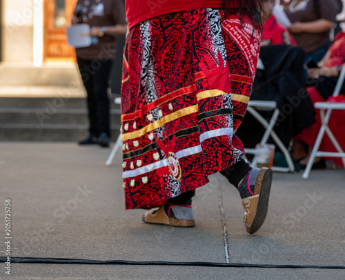 Close-up of a person wearing a traditional red ribbon skirt with MMIP (Missing and Murdered Indigenous Peoples) red handprint motifs. 