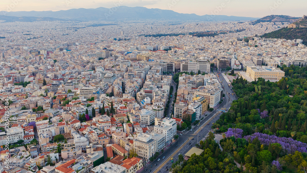 Obraz premium Athens urban landscape featuring the hellenic parliament building next to the lush national garden and a bustling avenue, extending towards distant mountains under a clear sky