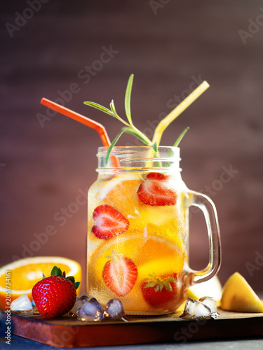 Refreshing cold summer detox water with strawberry, orange, lemon slices and ice. Slices of berries and fruits on the table