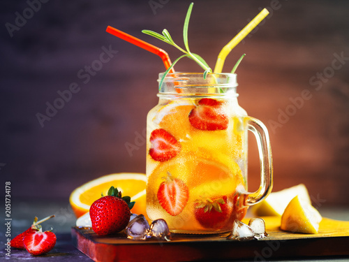 Refreshing cold summer detox water with strawberry, orange, lemon slices and ice. Slices of berries and fruits on the table