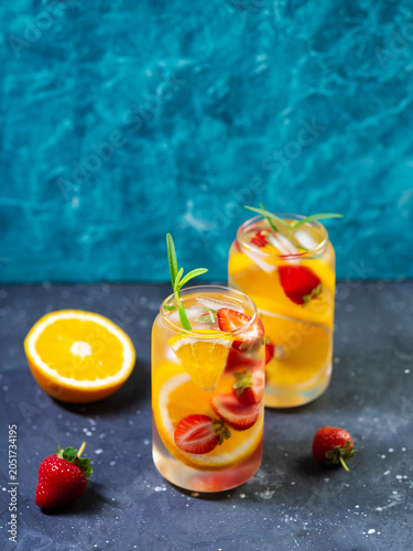 Two glasses of Refreshing cold summer detox drink with orange and strawberry. Blue background