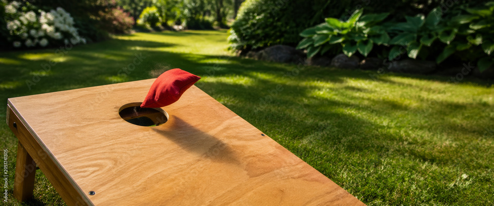 Obraz premium Red bean bag flying towards hole in cornhole board
