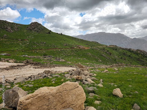 Lush green spring hills with large boulders, melting snow patches, and rocky terrain under partly cloudy sky
📍 Hawraman Takht, Kurdistan, Iran 