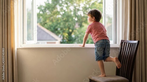 Unsupervised young child standing barefoot on a dining room chair while dangerously leaning out an open window, representing curiosity, childhood hazards, and the need for home safety