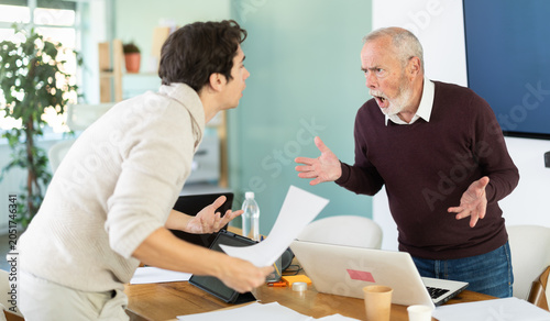 Cuadro en lienzo Elderly and young men colleagues around table engaged in heated argument in tens