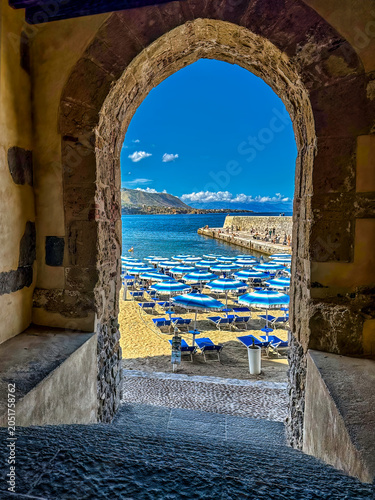 View of Cefalù beach through a stone archway in Sicily, Italy