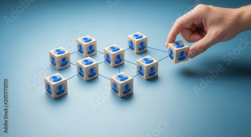 Hand connecting wooden cubes with user icons to form network diagram on blue background