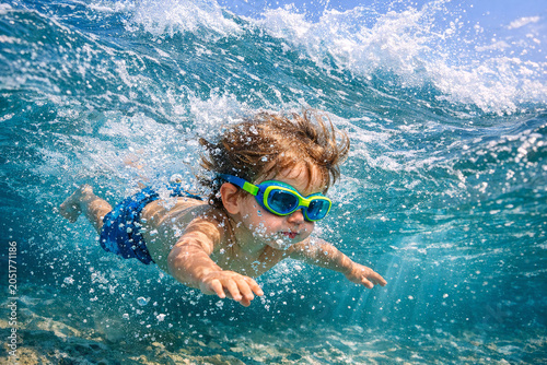 The image shows a young child wearing goggles and flippers, engaging in swimming activities with ocean water around them.