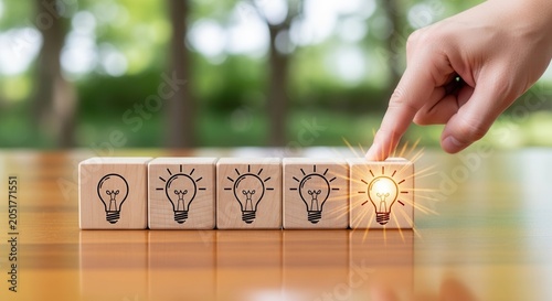 Hand pressing glowing light bulb icon on wooden blocks symbolizing idea generation and innovation