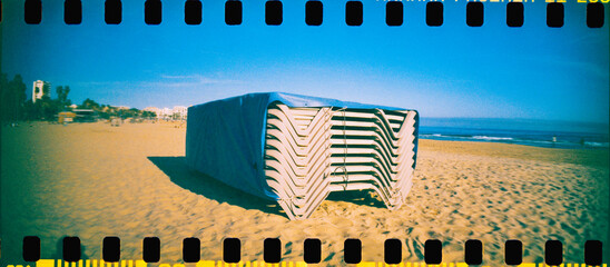 stacked beach loungers under a blue tarp by the sea, 35mm film