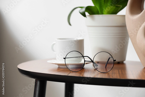 Canvastavla Stylish round eyeglasses with coffee cup and plant on table in room, closeup