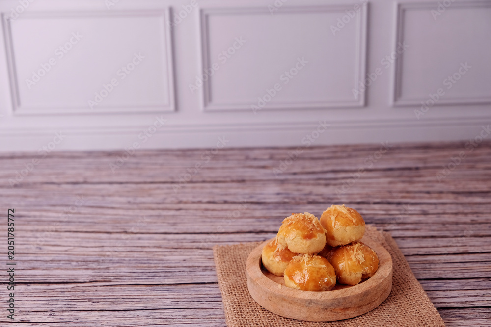Fototapeta premium Kue Nastar or Golden pastries rest in a wooden bowl. Bowl sits atop burlap on aged wood. Warm tones evoke comfort and homemade charm. Ideal for food blogs, bakery ads, or cozy lifestyle content