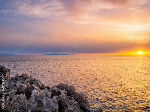 Coucher de soleil dramatique orange-rose sur mer calme avec rochers silhouettés au premier plan