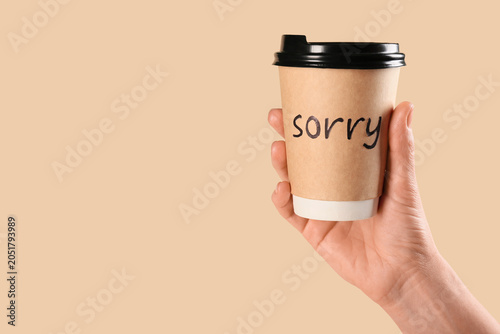 Foto Hand with paper cup of coffee with word SORRY on beige background