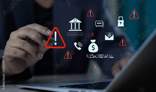 Businessman using laptop with bank fraud warning hologram. Financial scam detection and cybersecurity alert icons on money, email phishing, and phone risk.