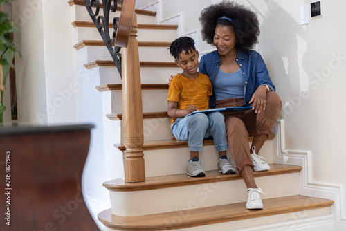 African American mother and child sitting on wooden staircase reading children's book near newel