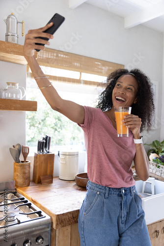 Smartphone resting next to glass of orange juice on wooden countertop in home kitchen with utensils
