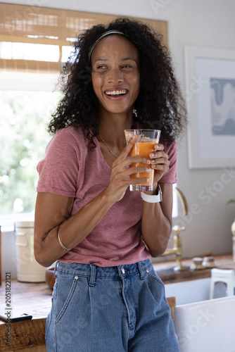African American woman leaning against wooden kitchen counter holding glass of orange juice