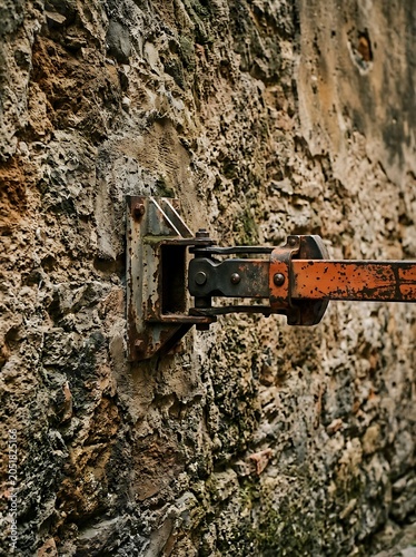 Rusty Orange Metal Arm Attached to an Old Stone Wall