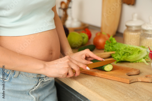 Young pregnant woman cutting cucumber for preparing fresh vegetable salad in ...