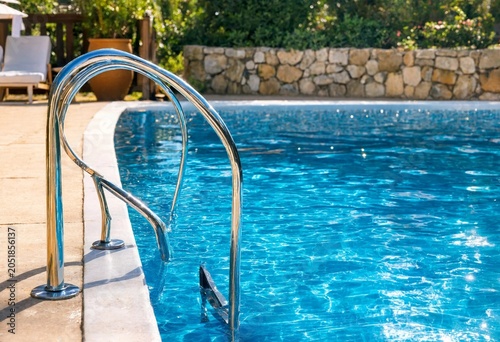 Crystal clear blue swimming pool water with shimmering sunlight reflections, elegant steps, refreshing ripples, luxury resort atmosphere, summer vacation, wellness, relaxation, travel.