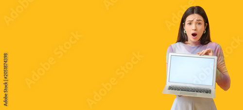 Obraz na płótnie Shocked young woman with blank laptop on yellow background