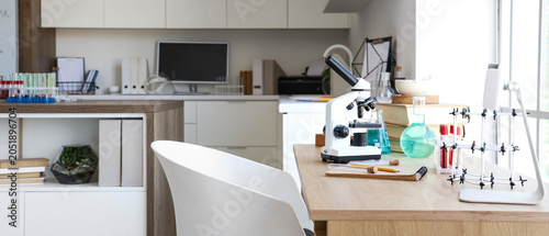 Chemical glassware, notebook and microscope on table near window in medical l...