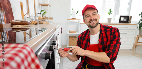 Male technician with screwdriver repairing oven in kitchen