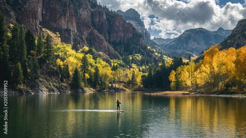 Paddler on mountain lake surrounded by autumn foliage and forest with mountains