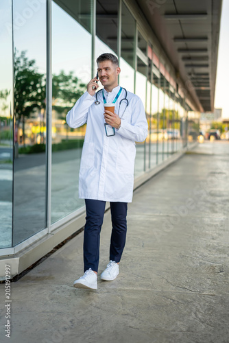 Foto Male doctor walking, talking on phone, drinking coffee