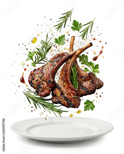 Two grilled lamb chops floating above a white plate with fresh herbs and seasoning spices