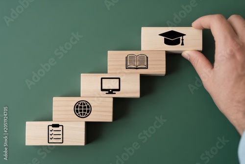 Hand stacking wooden blocks with education icons on green background